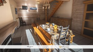 Un comedor con una larga mesa de madera, bancos y una araña. Se ve una escalera al fondo.