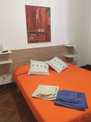 Quarto de hotel com cama, almofadas, manta e um quadro na parede.