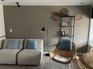 A modern living room with a sofa, a wicker chair, a floor lamp, and decorative wall art. - Het Paalhoofd 3 personen  (Westkapelle)