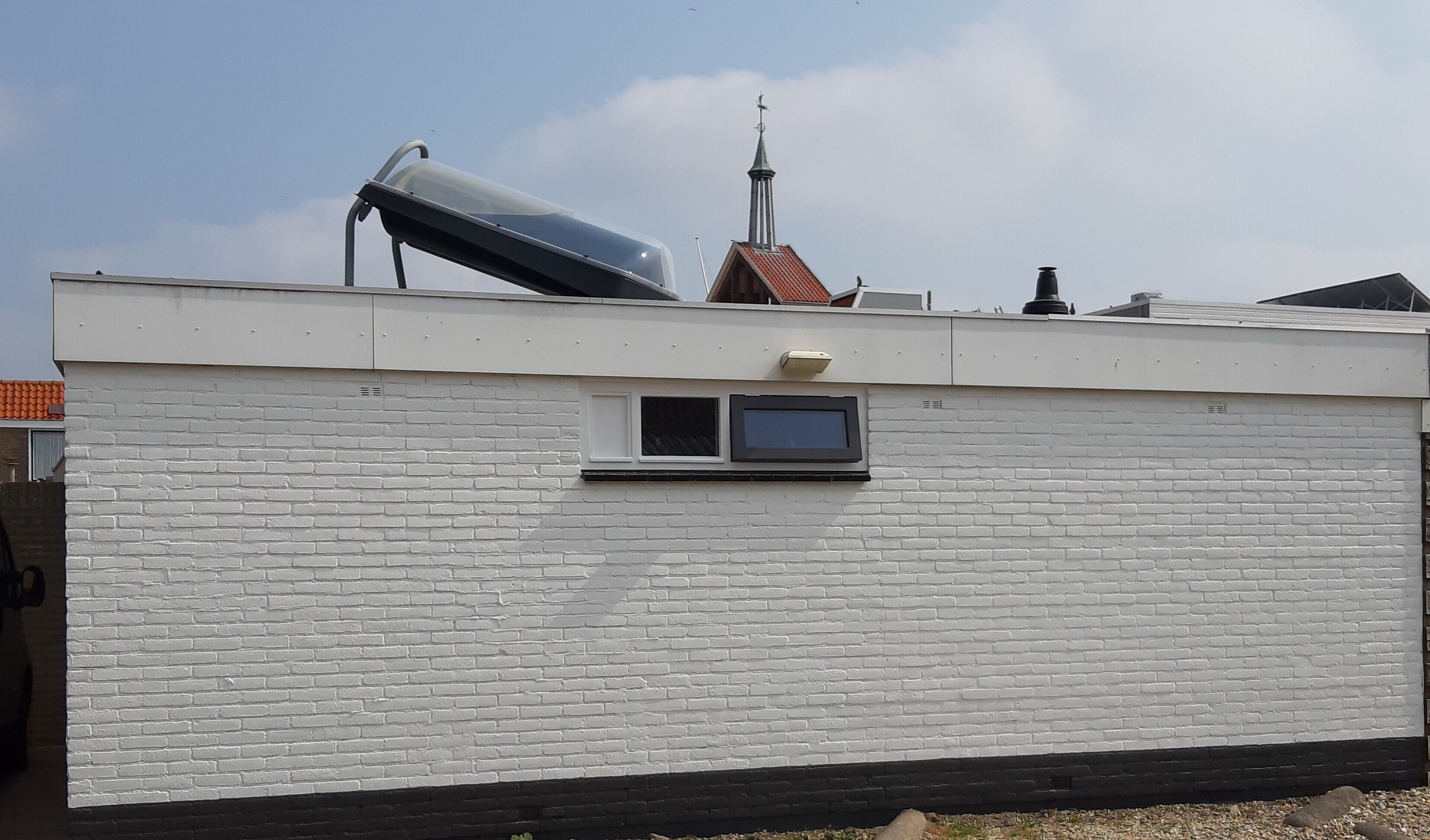 Un edificio con fachada de ladrillo blanco, una ventana pequeña y una chimenea.