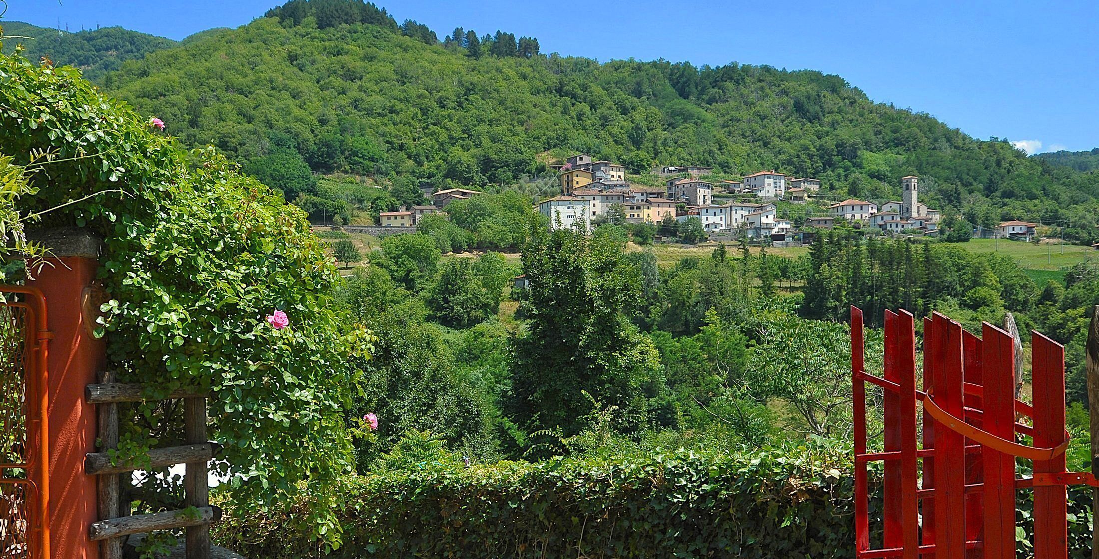 Ein Dorf an einem Hang mit traditionellen Häusern, üppiger Vegetation und blauem Himmel.