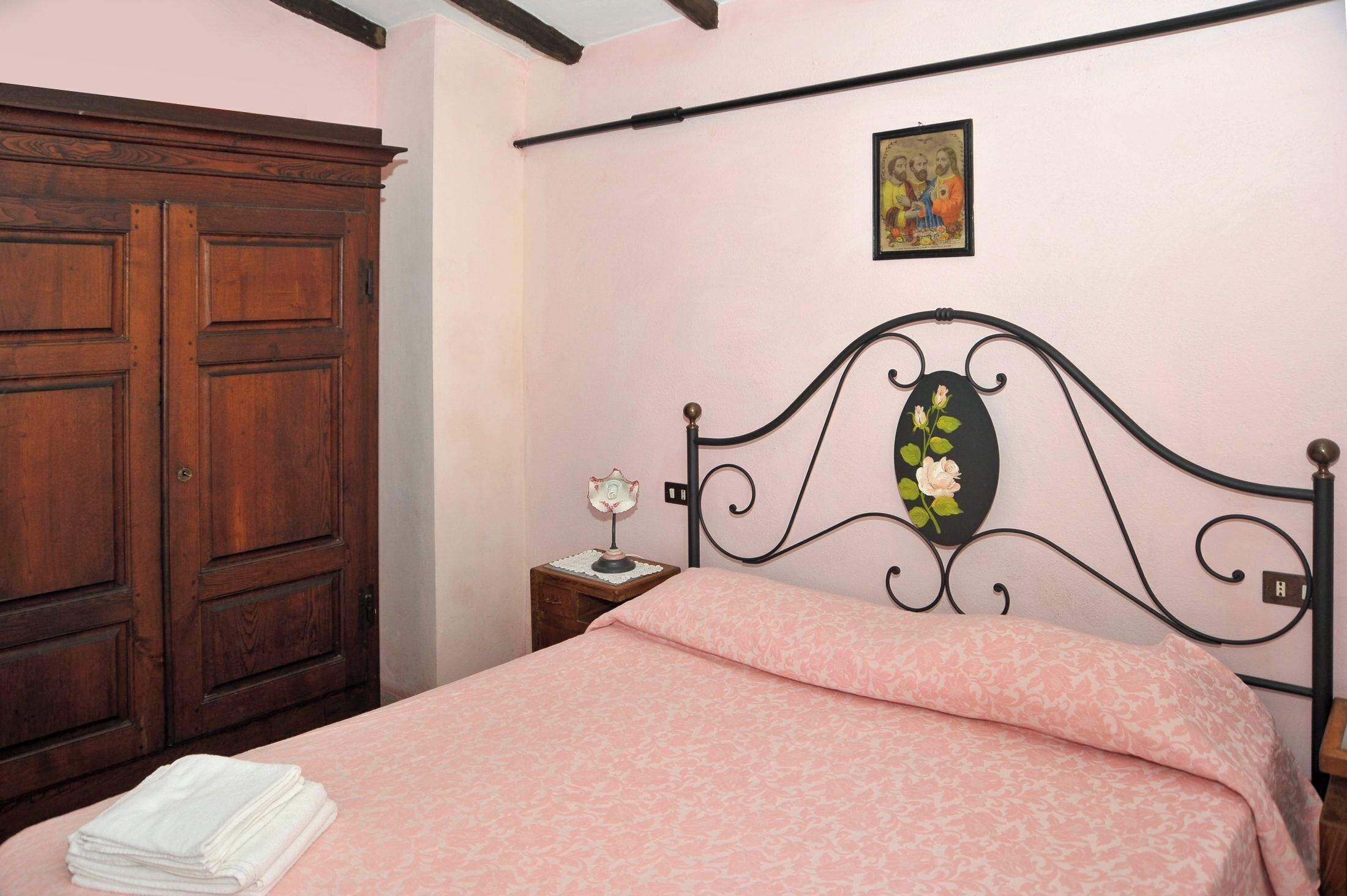 A bedroom with a bed, a wooden wardrobe, a nightstand with a lamp, and a wall-mounted picture.