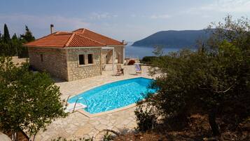 A stone house with a tiled roof, a swimming pool, and a view of the sea.