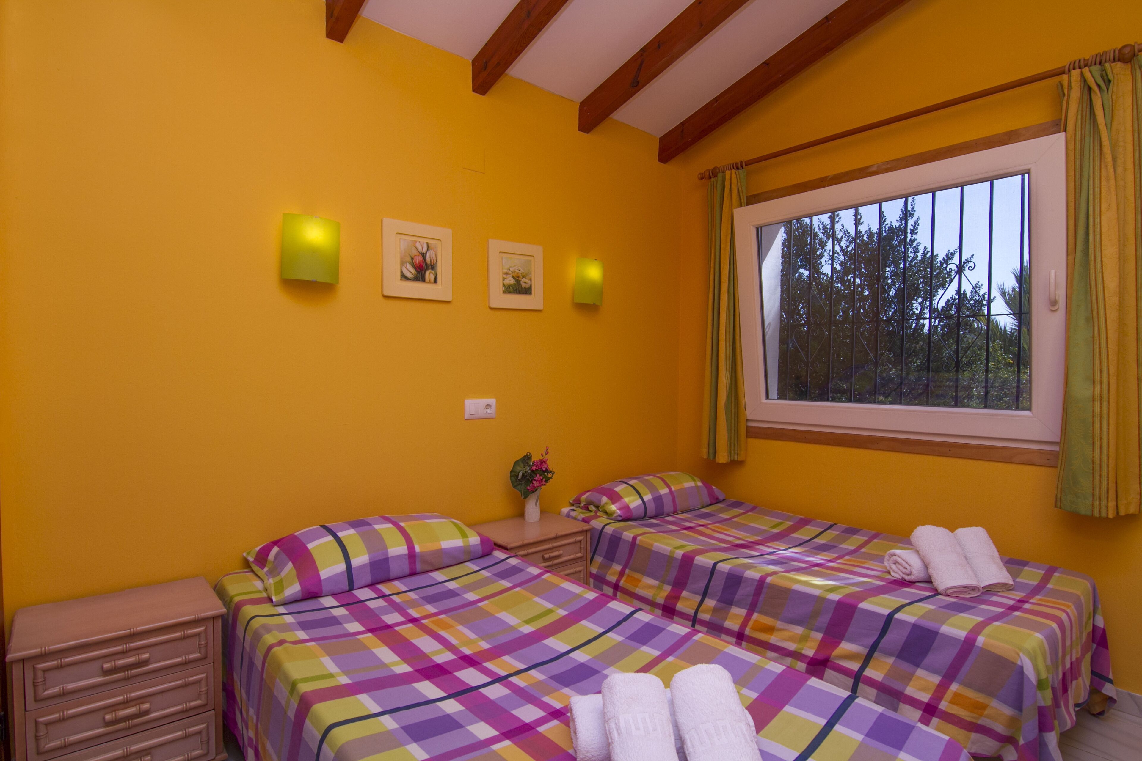 Une chambre avec deux lits, une table de chevet, une commode et une fenêtre avec des rideaux.