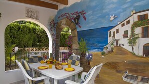 A dining area with a mural of a coastal scene, a table with chairs, and a view of the outdoors. - Promana -Villa Ricarda with private pool 850m to the sea between Moraira & Calpe (Benissa)