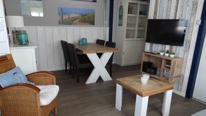 Uma sala de estar aconchegante com móveis de vime, uma mesa de jantar de madeira e uma televisão de tela plana.