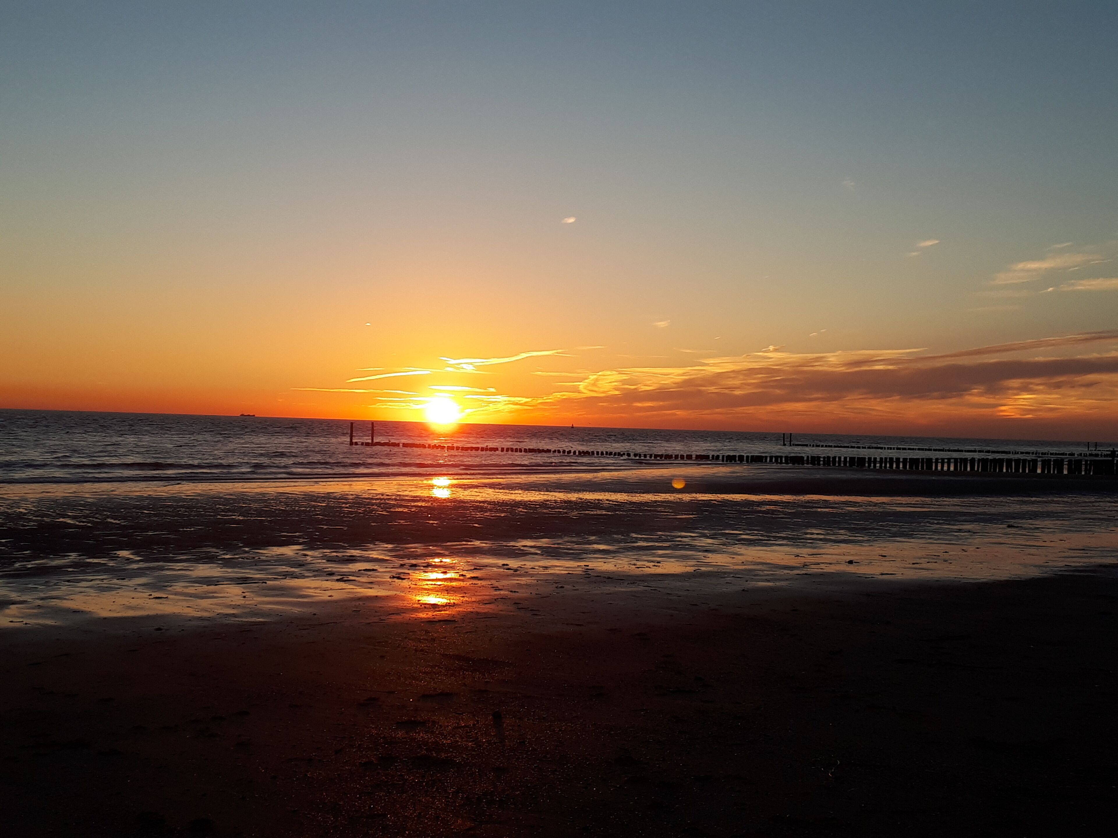 Un coucher de soleil sur une plage, avec une jetée qui s’avance dans l’eau.