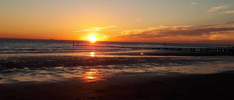 Un coucher de soleil sur une plage, avec une jetée qui s’avance dans l’eau.