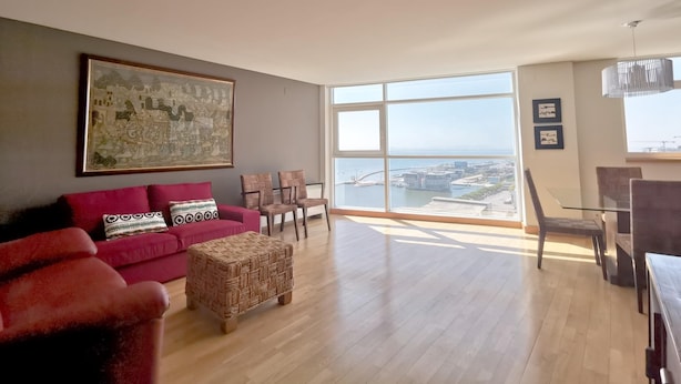 A spacious living room with a large window offering a view of the sea and cityscape.