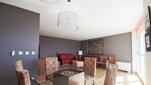 A modern living room with a glass coffee table, woven chairs, a red sofa, and a large painting on the wall.