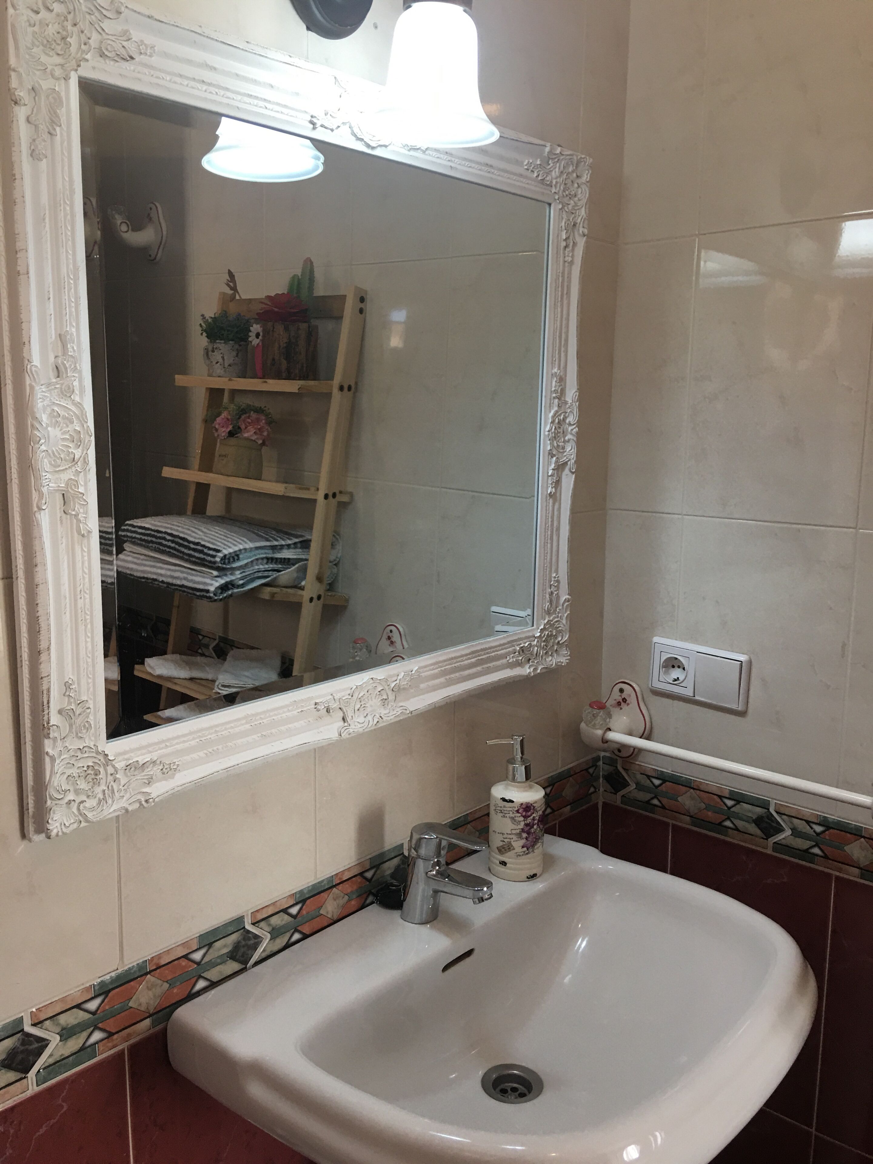 A bathroom with a white sink, a mirror with an ornate frame, and a tiled backsplash.