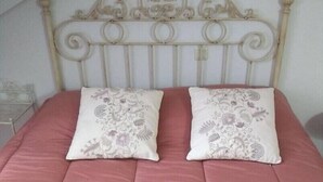 A bed with a pink bedspread and two decorative pillows, a white metal headboard, and a white wall. - ACCOMMODATION IN PEDRAZA - MERCHE 1 (Pedraza)