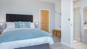 A modern bedroom with a large bed, bedside lamps, a wooden door, and a glass shower area. - Luxury Apartment - Sleeps 4 -  Spectacular Views with Private Pool and Hot Tub   (Torquay)