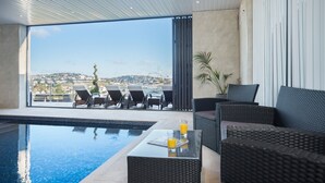 A modern indoor pool area with a view of a cityscape, furnished with lounge chairs and a sofa. - Luxury Apartment - Sleeps 4 -  Spectacular Views with Private Pool and Hot Tub   (Torquay)