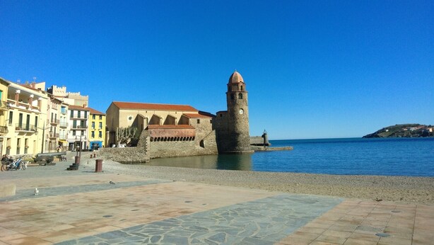 A coastal town with a prominent tower, a paved square, and buildings along the waterfront. - Luxury Apartment (Collioure)