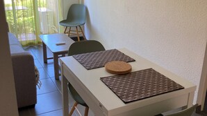 A dining area with a white table, two chairs, and a cork coaster. A green chair is visible in the background. - Luxury Apartment (Collioure)