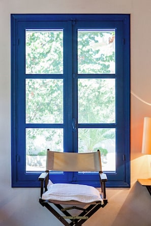 A chair positioned in front of a blue-framed window with a view of greenery.