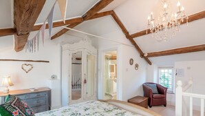 A bedroom with a bed, dresser, chair, and chandelier. - Wonderful Grade II Cotswold Stone Cottage in Perfect Location (Chipping Campden)