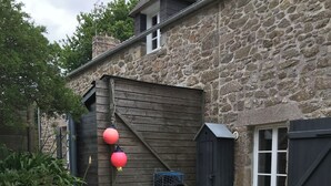 A stone house with a wooden door, a small shed, and a garden with plants and a gravel path.
