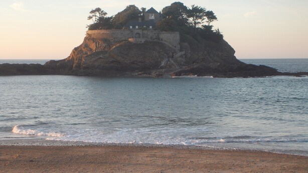 A beach with a rocky outcrop and a building on top.