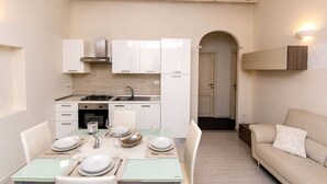 A compact kitchen with white cabinets, a stove, and a dining area with a table set for two. - Brigata House-Luxury 2 bed apartment with sea views, close to sea and shops,wifi (Castelsardo)
