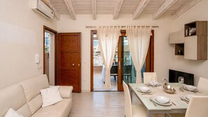 A modern living room with a sofa, dining table set for four, and a view through a glass door to an outdoor patio. - Brigata House-Luxury 2 bed apartment with sea views, close to sea and shops,wifi (Castelsardo)