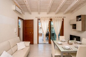 A modern living room with a sofa, dining table set for four, and a view through a glass door to an outdoor patio.