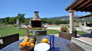 Ein Essbereich im Freien mit Grill, Korbstühlen und Blick auf Pool und Berge.