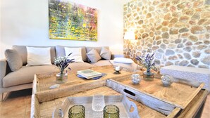Ein Wohnzimmer mit einem beigefarbenen Sofa, einem Couchtisch aus Holz mit Dekoration und einem farbenfrohen abstrakten Gemälde, sowie einer Steinwand.