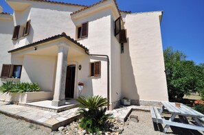 A two-story building with a tiled roof, a stone-paved entrance, and a small garden area with plants and a wooden bench. - Villa SON RUBI in Serra de Tramuntana with BBQ & private pool. It's very popular-Villaonline- - Free Wifi (Selva)