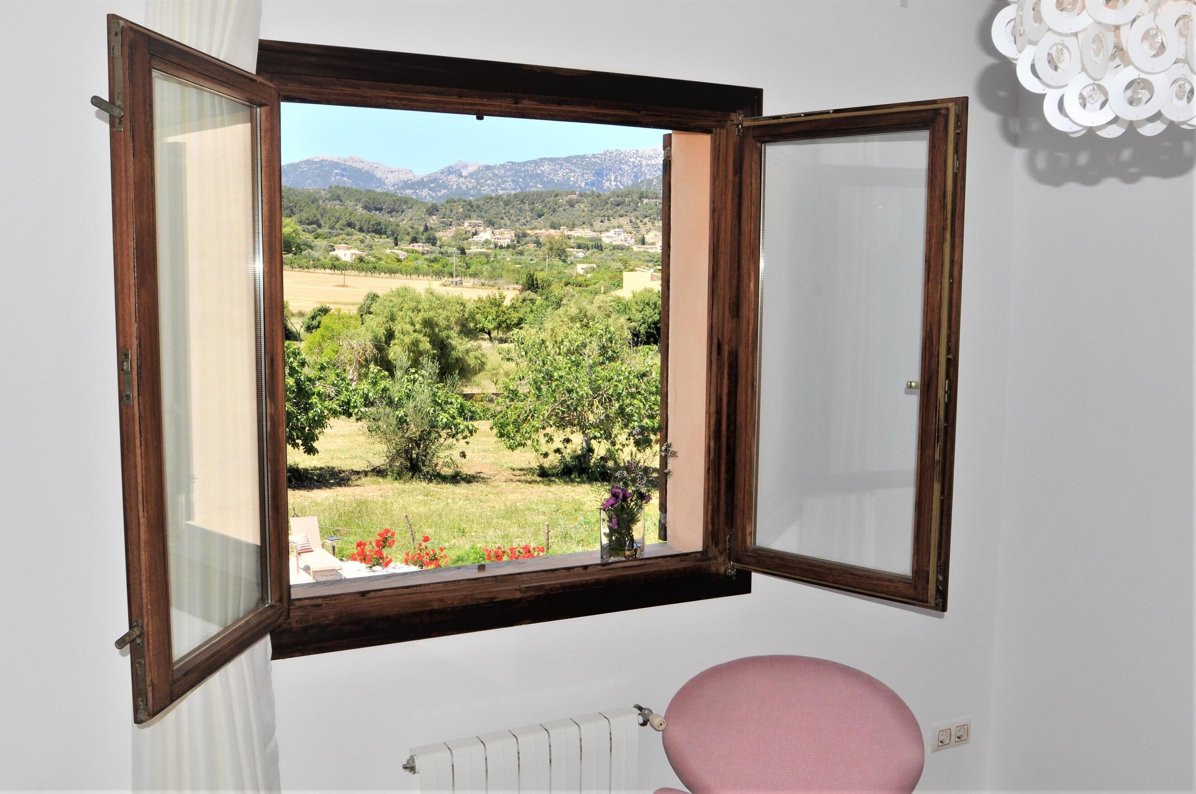 Habitació amb finestra que ofereix vistes a un paisatge de muntanya i un poble.
