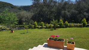 A garden with a stone wall, a wooden fence, and a clear view of a hilly landscape. - Rent Villa In Corfu, Private Pool, Luxurious, Gorgeous Views, In House Catering (Klimatia Karousades)