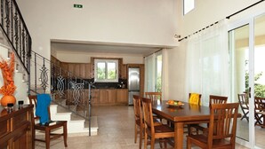 A spacious dining area with a wooden table and chairs, a kitchen in the background, and a staircase leading to another level. - Rent Villa In Corfu, Private Pool, Luxurious, Gorgeous Views, In House Catering (Klimatia Karousades)