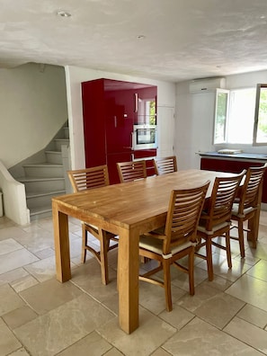 A dining area with a wooden table and chairs, a red kitchen with appliances, and a window with a view.