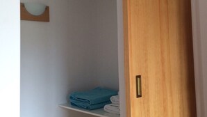Une porte en bois donne sur un placard où se trouvent des étagères remplies de serviettes pliées et une serviette bleue.