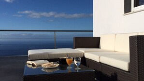 Un balcon avec un canapé en osier, une table en verre et une vue sur l’océan.