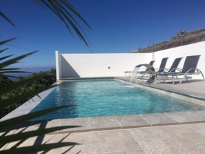 A swimming pool with clear blue water, surrounded by a white wall and a few lounge chairs. - Secluded villa boasting panoramic views to the sea - infinity pool and free Wifi (Tijarafe)
