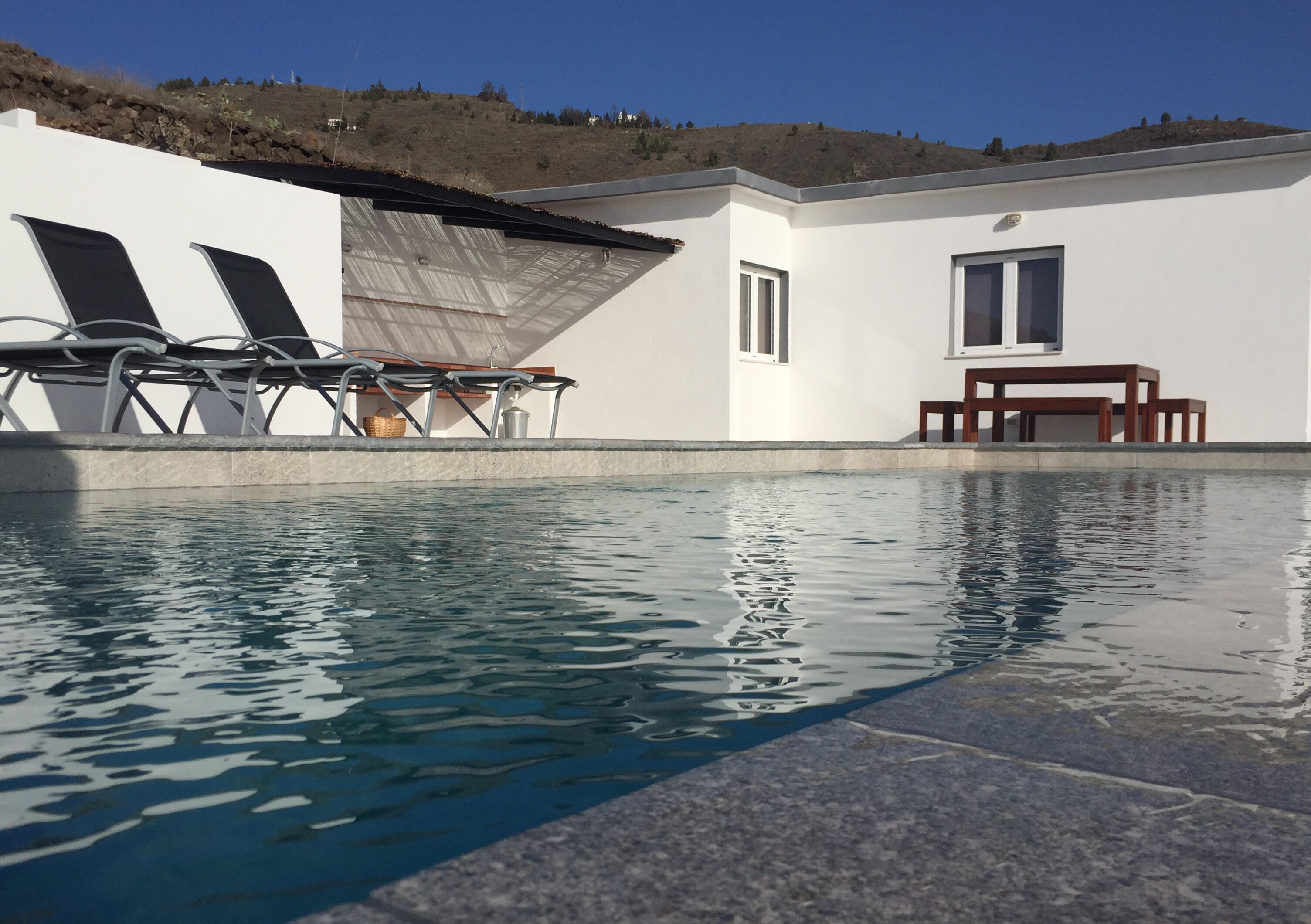 Ein Swimmingpool mit Liegestühlen und einem Tisch, umgeben von einem weißen Gebäude mit Fenster und Tür.