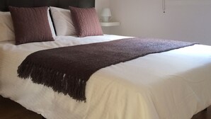 Un lit avec une tête de lit sombre, une literie blanche et un plaid marron.