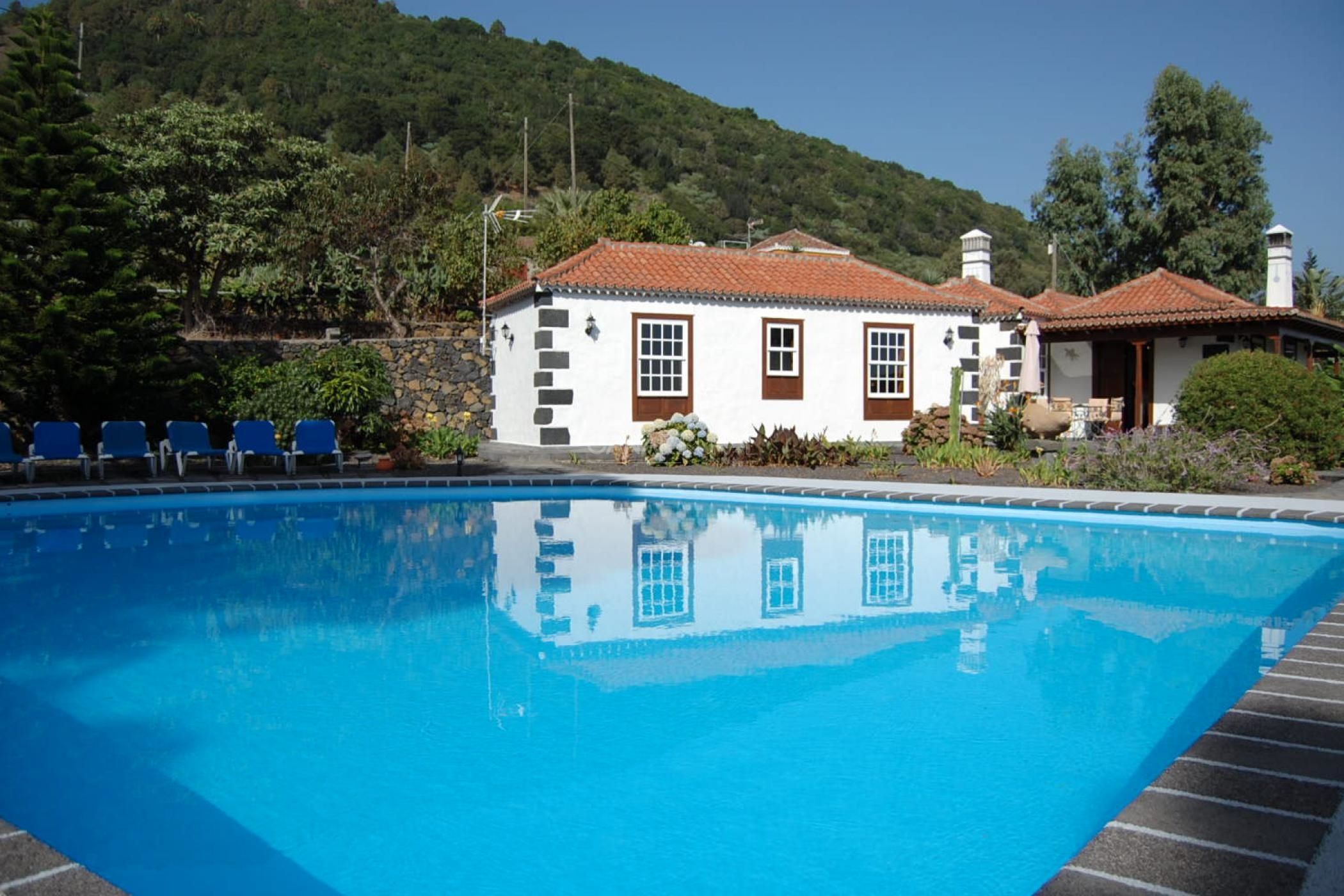 A swimming pool with a white building with brown trim in the background.