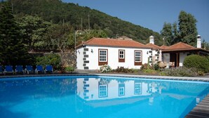 Piscina com um edifício branco e detalhes em castanho ao fundo.