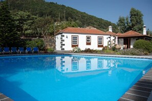 Piscina com um edifício branco e detalhes em castanho ao fundo.