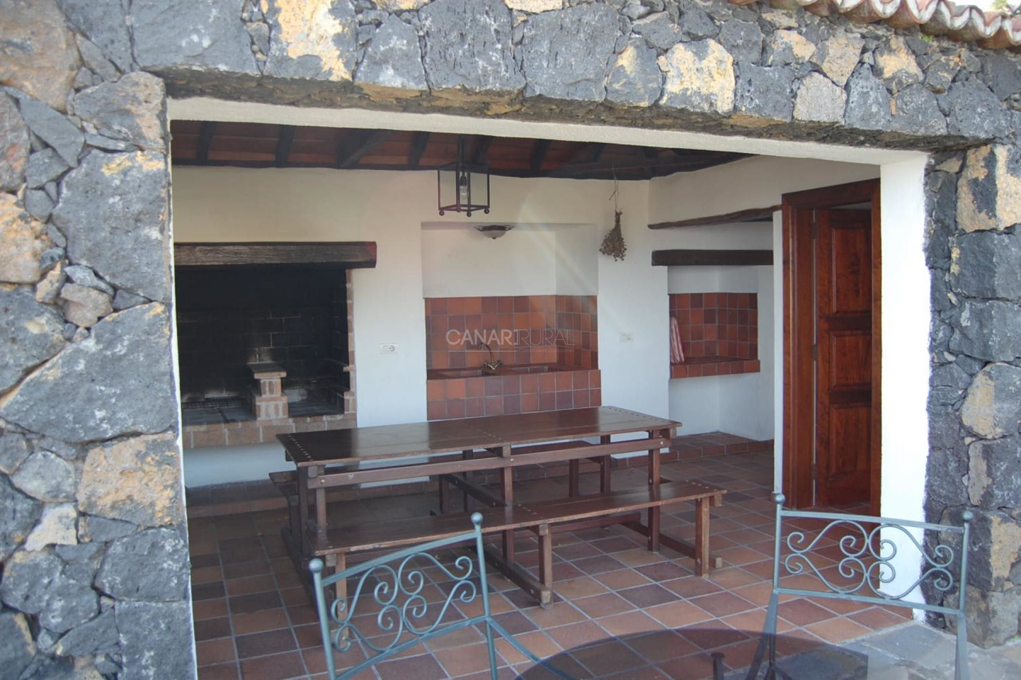 A stone-walled room with a tiled floor, a wooden table, and a bench.