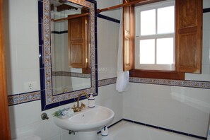 Casa de banho com uma pia branca, espelho e armários de madeira.