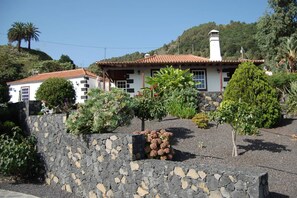 Una casa con un muro in pietra, un tetto in tegole e un giardino con diverse piante.