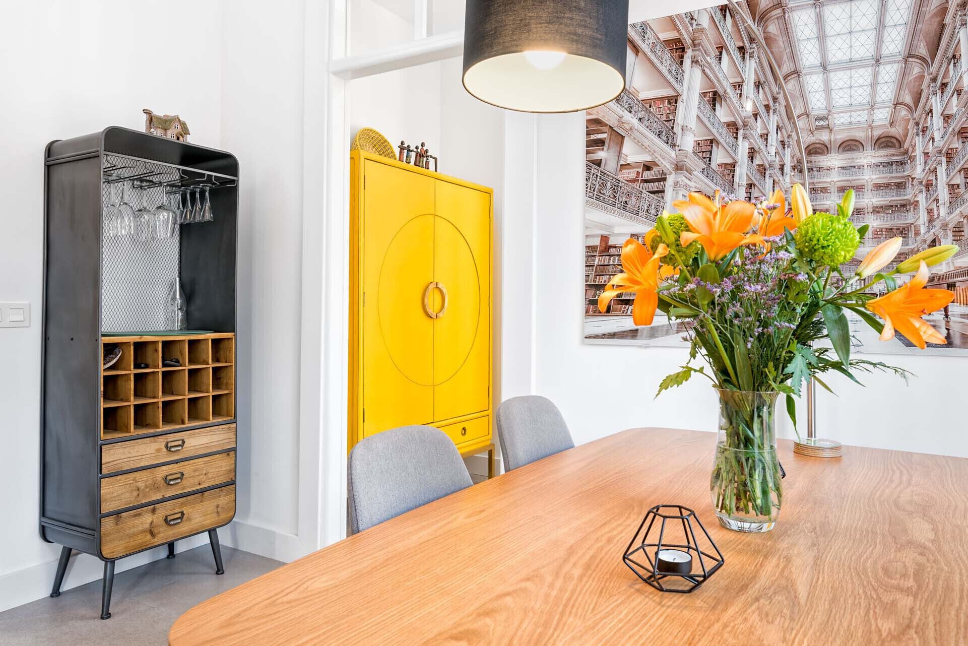 A dining area with a wooden table, a yellow cabinet, and a vase with flowers.