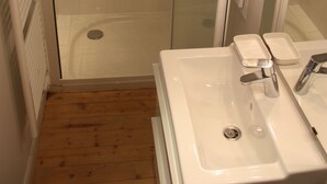 Een badkamer met een douchecabine van glas, een witte wastafel en een spiegel met verlichting.