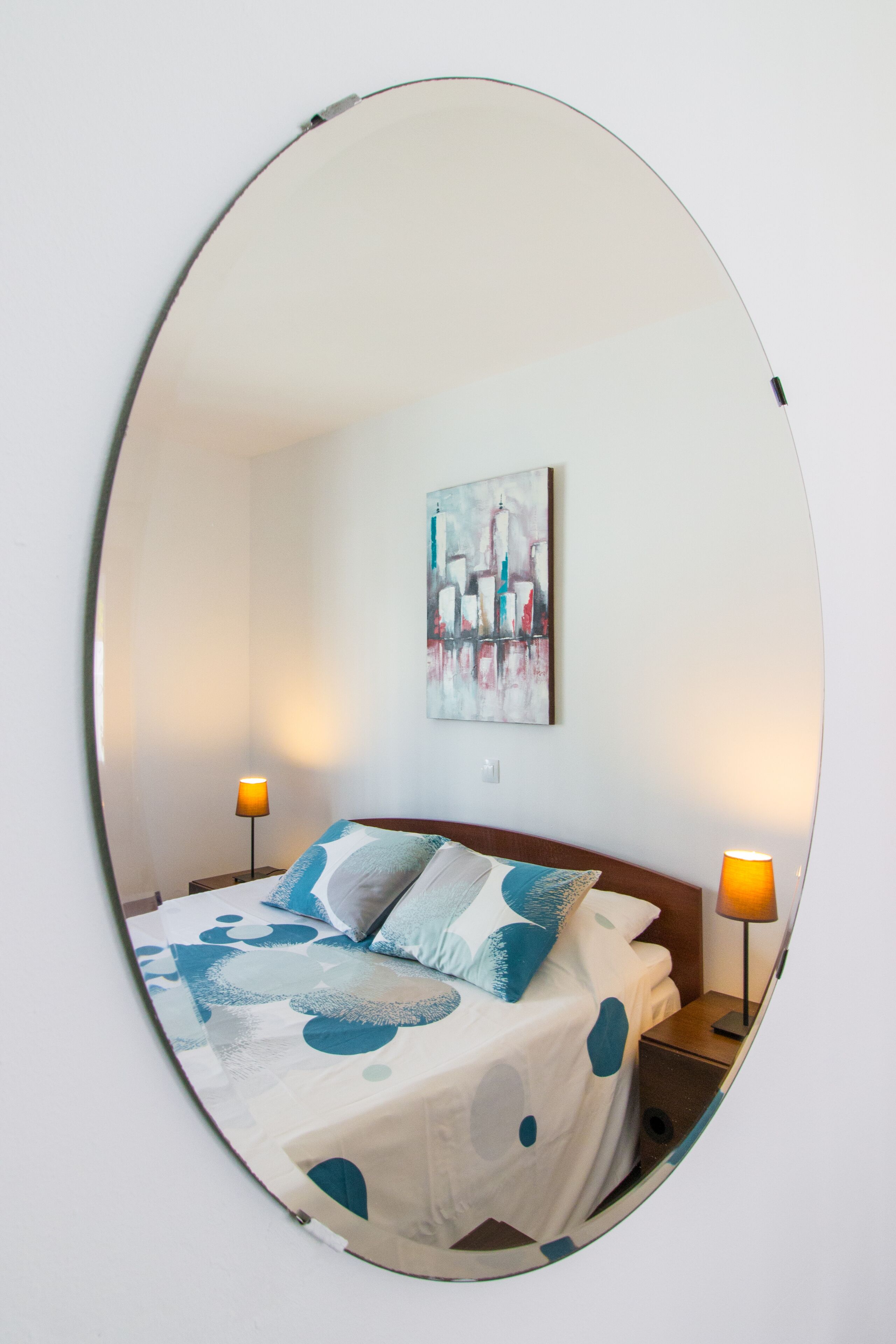 Habitación de hotel con una cama, dos lámparas de noche y un cuadro de paisaje urbano en la pared.