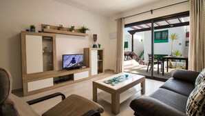 A modern living room with a sofa, coffee table, TV, and shelves with plants.