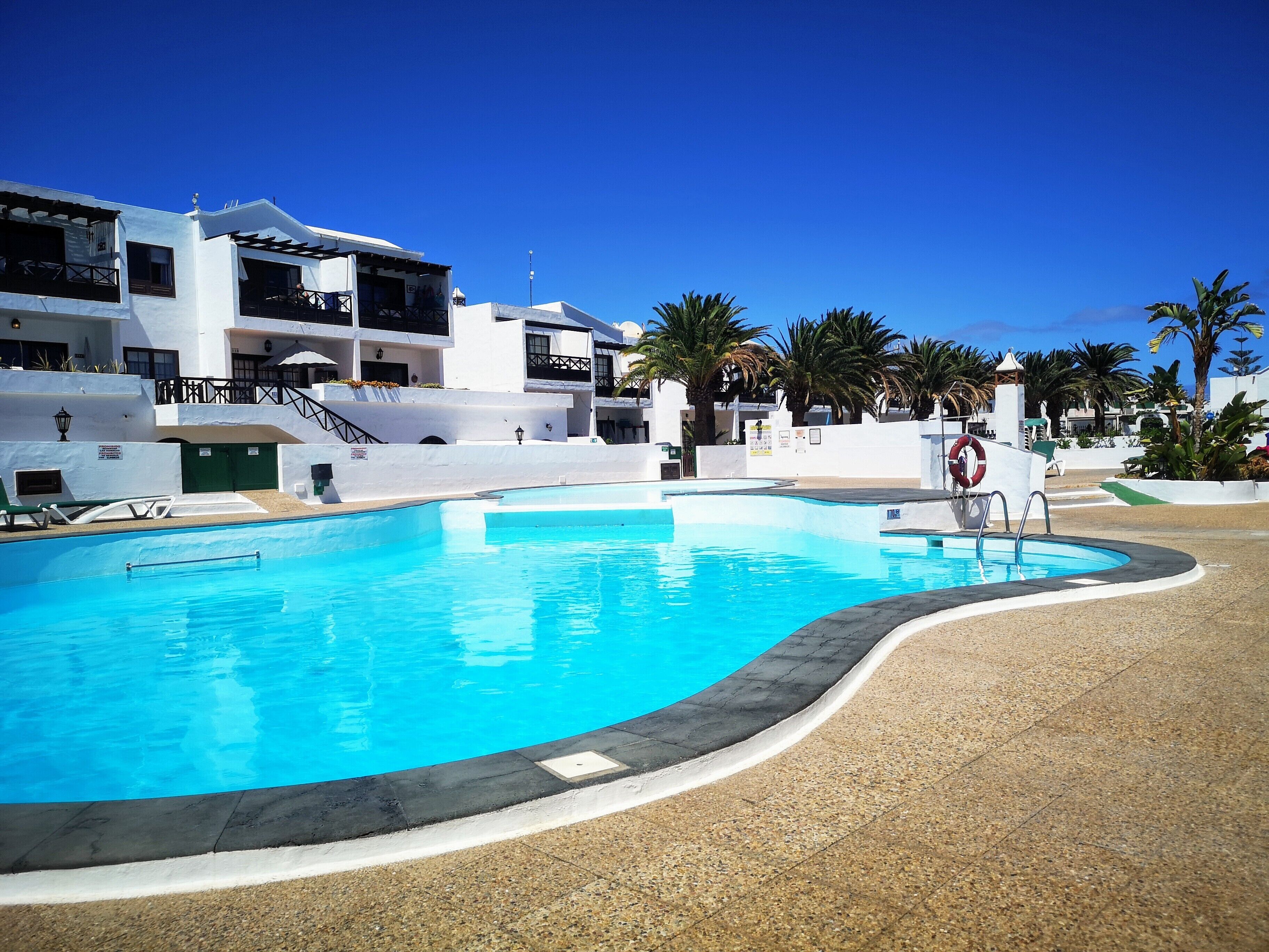 Ein Pool mit geschwungener Kante, umgeben von einem Kiesweg. Liegestühle und ein Rettungsring befinden sich in der Nähe.